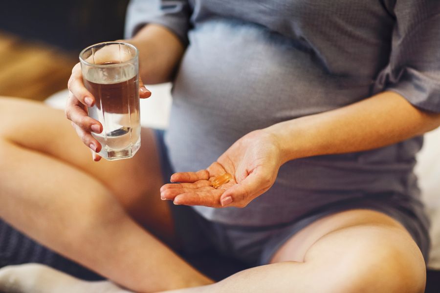 Pregnant woman holding a cup of water and a pill